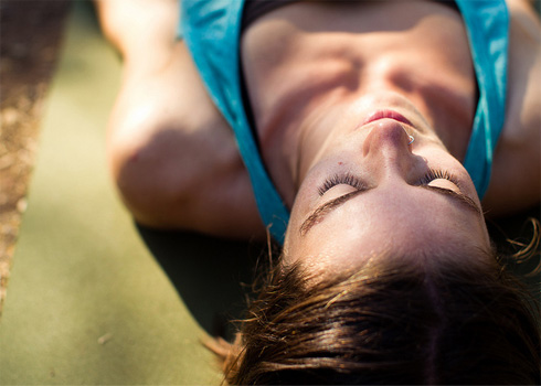 female lying down on yoga mat with filtered sunlight on her face